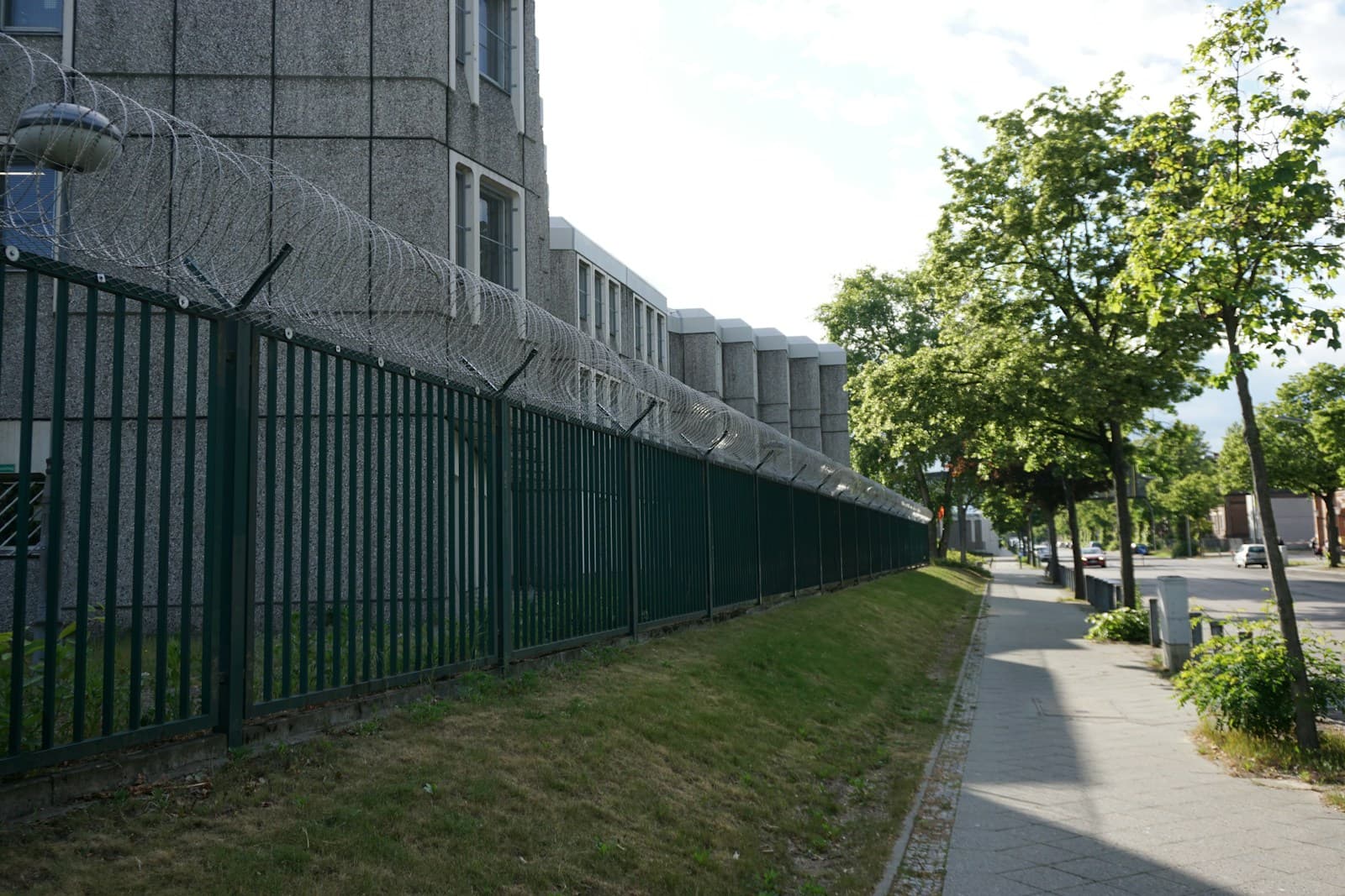 A low building behind a tall perimeter fence under a grey sky